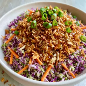 Top-down view of crunchy ramen noodle salad featuring jagged toasted noodles and shredded purple cabbage. (ramen noodle salad)