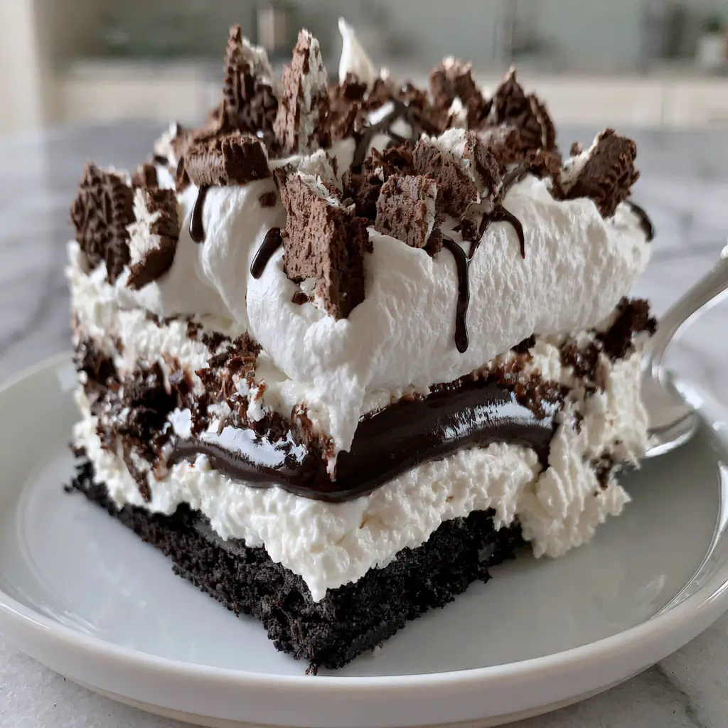 A single square slice of the no bake oreo dessert on a white plate with dark chocolate drizzle and jagged cookie chunks.