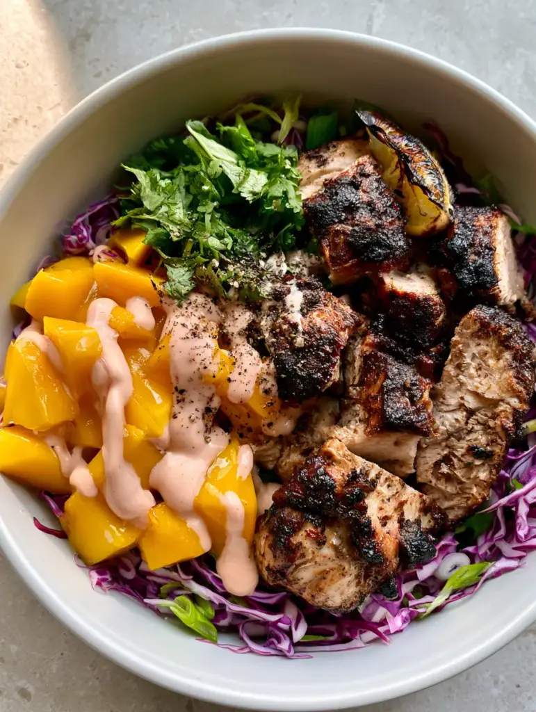 Jerk Chicken & Mango Slaw Bowls with Creamy Honey-Lime Drizzle 1 A vibrant meal prep bowl with shredded purple cabbage, scallions, and a pale-pink creamy drizzle.