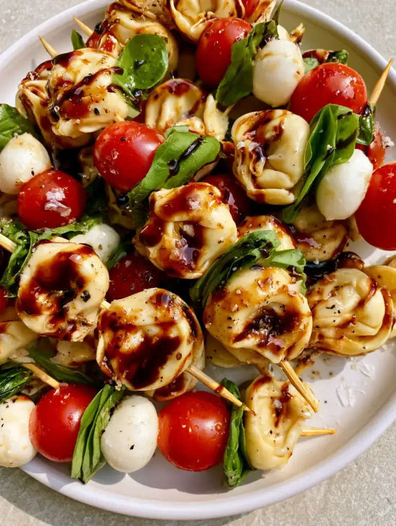 Elegant appetizer display of Caprese Tortellini Skewers on a grey stone countertop featuring fresh basil and sea salt flakes.