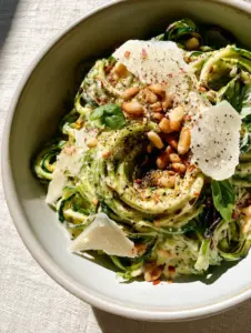 Close-up of emerald green Zucchini pasta strands with charred edges and silky white sauce.