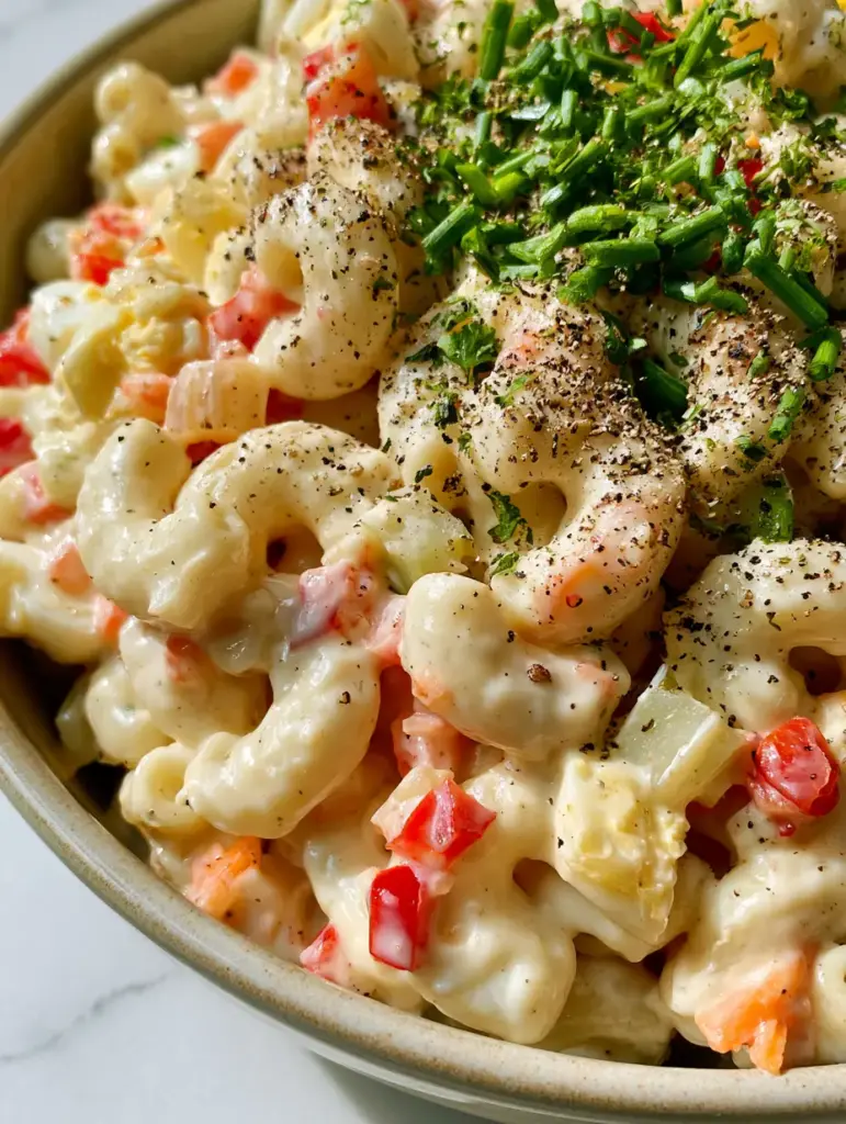 Deli Macaroni Salad: The Creamiest Ultra-Glossy Recipe 1 Deli macaroni salad featuring chunks of hard-boiled eggs and vibrant shredded carrots on white marble.