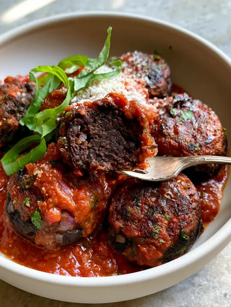 Vegan Black Bean Meatballs with a Crispy Seared Crust 1 A silver fork splitting a vegan black bean meatball in half to reveal a firm, dense interior that is perfectly set.